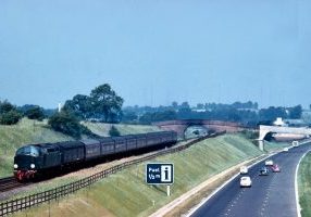 In 1960, un-named English Electric Type 4 No. D216 (named Campania in May 1962) heads South on an express to Euston, unusually with an LNER-design gangwayed brake leading the formation, alongside the newly-opened M1 motorway. In the background can be seen the Daventry radio masts where, in 1935, Robert Watson-Watt and Arnold Wilkins carried out their famous demonstration of the detection of an aircraft by radio echoes - and the invention of radar. Photo: Derek Cross, courtesy David Cross.