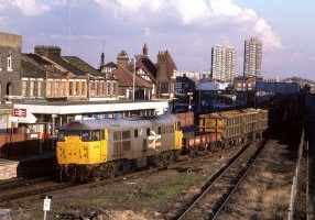 Early-bodied Class 31 No. 31108 has propelled its short consist of scrap and a single SPA wagon from Ward's Siding along the Silvertown Tramway, reversed in the headshunt and is seen accelerating past the single-platform station as it heads towards Temple Mills with 6C97 on 22nd October 1987. Photo: Alan Jones