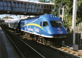 For the 2000 Olympic Games in Sydney, it was entirely appropriate for conveniently numbered power car 2000 to be chosen to promote them. Here we see it at Hornsby in the early morning sun making its pick-up stop on its way to Brisbane in December 2000. 
Hornsby is an important junction on the Sydney rail network. It is where the suburban North Shore Line (out of sight to the left) which has come from Sydney Central via the Harbour Bridge meets the main line to the north which has come from Central via Strathfield, as this XPT has done. Image Credit: Rob Freeman (Illustrative only - may not be included in the presentation...)