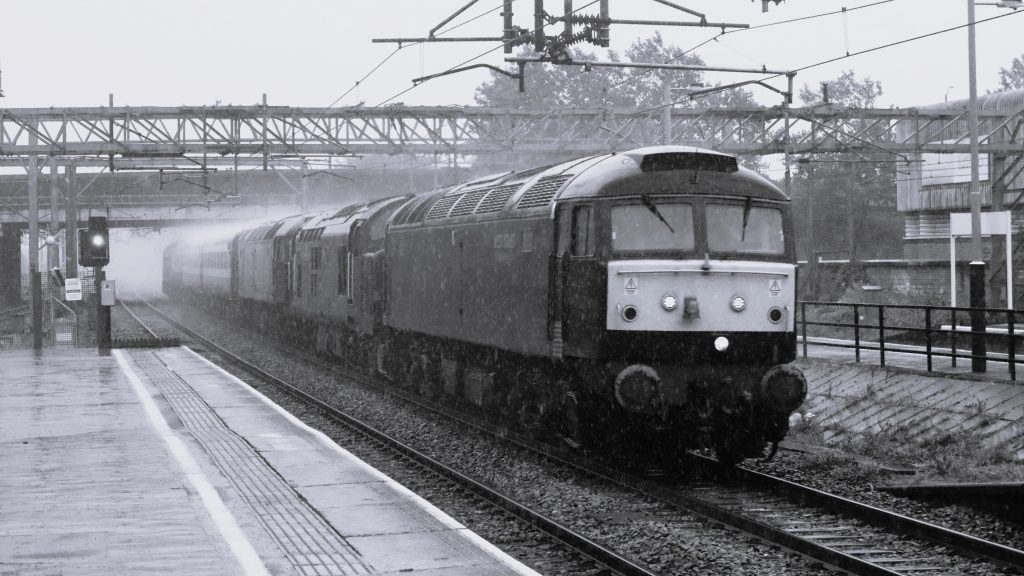 JPG-57003-leads-5M43-Southall-Carnforth The most interesting working of the day unfortunately coincided with a torrential downpour, though the spray and the use of monochrome have produced an image with good dramatic impact. 57003 heads 5M43, the 10.19 West coast Railways ECS from Southall to Carnforth. Behind the 57 are 37668 and 47484, while just visible at the rear is 33207. Image credit: Dale Robertson