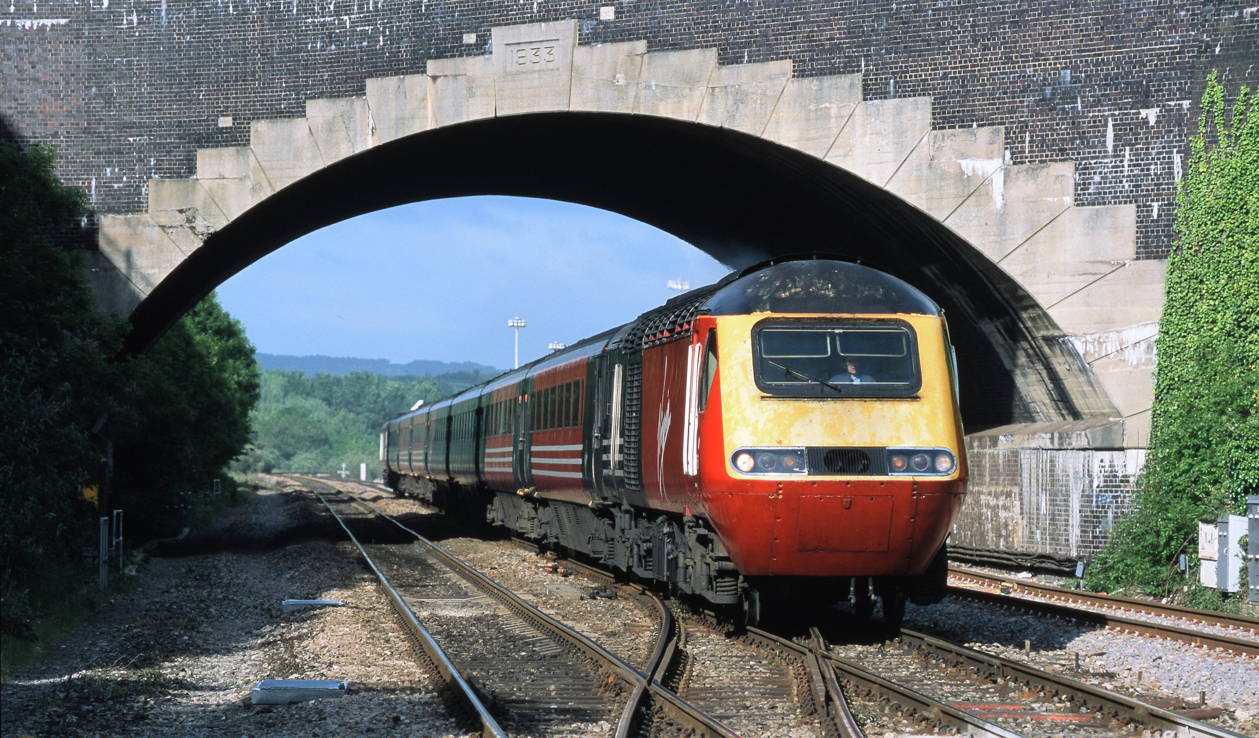 Headed by power car 43086, the 06.20 Plymouth to Newcastle 'Armada’ passes beneath the A38 road bridge at Parson Street on 31st May 2002.
The bridge was rebuilt in 1933 as part of a scheme to widen the railway through Bristol, which included construction of the platforms on the eastern side of Temple Meads outside the main overall roof.  Image credit: Stewart Jolly
