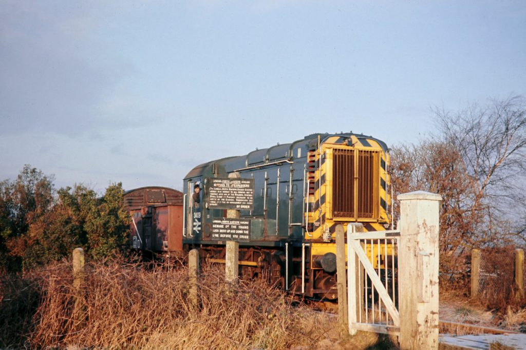 19701231-RAMSEY-St-MARYS-3409-08339-08 There were three gated crossings on the Ramsey North Branch: Whittlesea Mere, Long Drove and St Mary's Station, in order from Holme. At the first of these, Whittlesea Mere, March-allocated Class 08 No. 3409 has paused for the guard to open the gates whilst working 9B08, the 08.35 from Holme to Ramsey North on a cold and frosty, but beautifully sunny, 31st December 1970. The only intermediate station on the branch was Ramsey St Mary's (known as Holme St Mary's in the BR Working Timetable) which was an 'as required' stop for 9B08 and latterly generated little traffic. Photo: John Tolson, courtesy Trevor Davis.