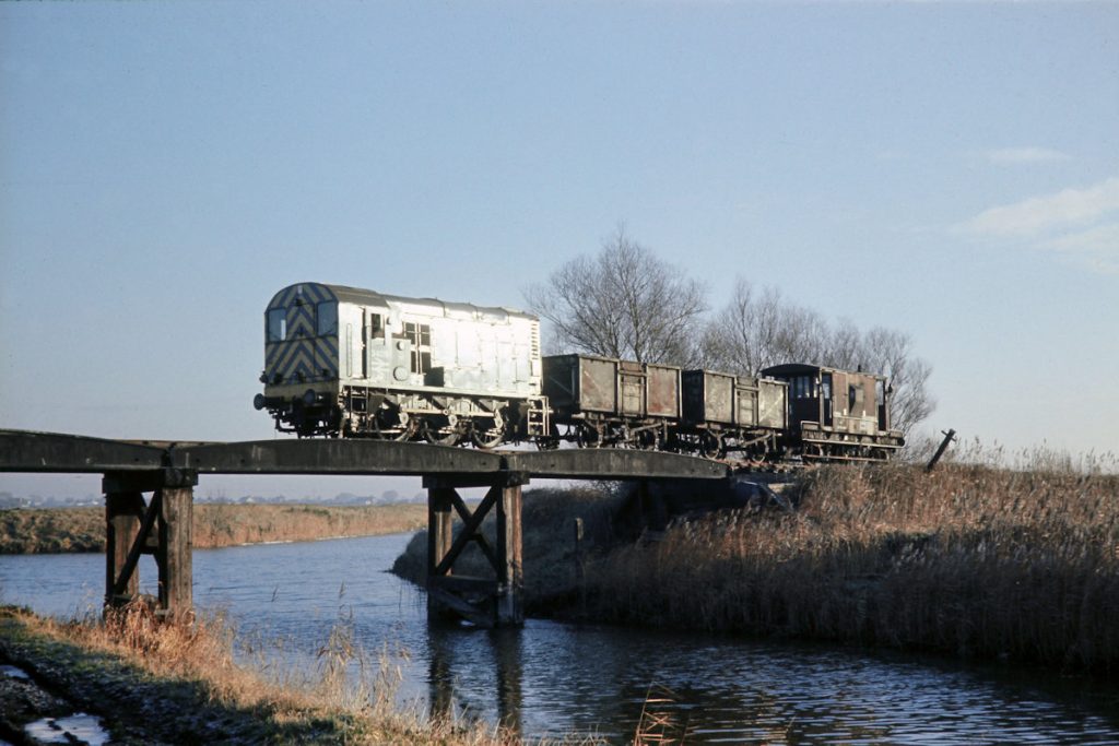 19701231-RAMSEY-St-MARYS-3409-08339-Crosses-New-Dyke-andjuntion-with-Old-River-Nene-with-Ramsey-North-to-Peterborough-Trip-Freight-JMT34906-John-Tolson-E3W The gradient profile of the Ramsey North branch was perfectly level apart from 1 in 66 inclines up to and down from the crossing of New Dyke, at its junction with the old course of the River Nene. Crossing New Dyke with two empty 16-ton minerals on 9B24, the 09.35 Ramsey to Holme, Class 08 No. 3409 (later 08339) catches the morning sun on December 31st 1970. Photo: John Tolson, courtesy Trevor Davis.