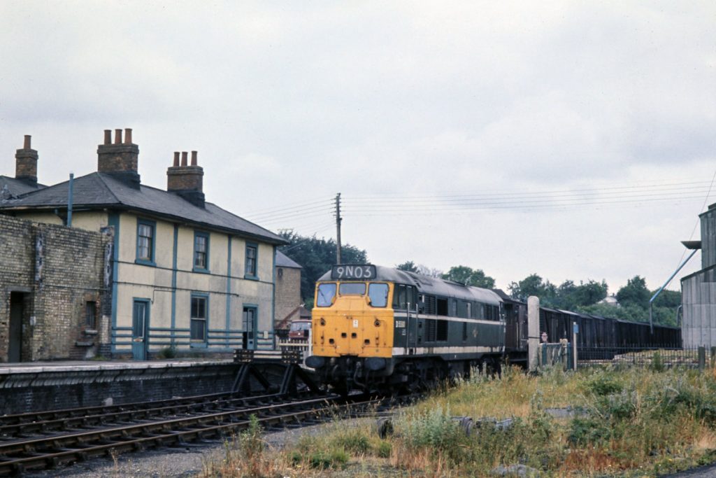 19700703-FAKENHAM-D5580-06 Making its way back to Wensum on Friday July 3rd 1970, Brush Type 2 No. D5580 (later 31162) eases over the level crossing and through the former station at Fakenham East. Although vacuum fitted, guards vans were retained on this and similar workings to assist with opening and closing the many level crossings which on branches such as Fakenham and Lenwade had lost their crossing keepers and were train crew operated. Photo: John Tolson, courtesy Trevor Davis.