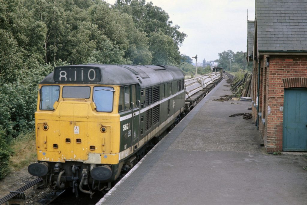 19700702-LENWADE-5621-16 Seen from the Signal Box steps at Lenwade, Brush Type 2 No. 5621 has collected four bolsters of reinforced concrete beams and begins its journey back to Norwich on July 2nd 1970. The headcode 8J10 is a little confusing as the letter J on the Eastern Region was used for trains destined for the Sheffield Division, but the Norwich Division also used J for trains to Whitemoor and Norwood Yard. Perhaps this indicates an independent spirit in Liverpool Street! Photo: John Tolson, courtesy Trevor Davis.