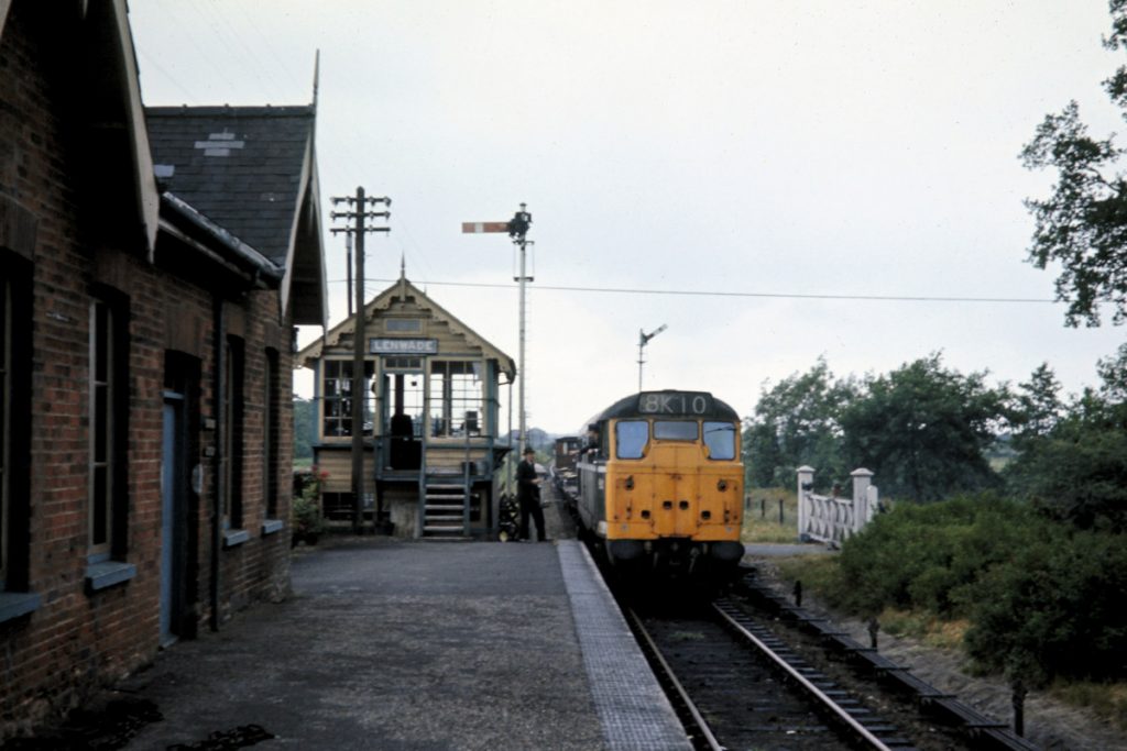 19700702-LENWADE-5621-Arriving-with-Freight-from-Norwich-JMT34940-John-Tolson-E4W On a dull July 2nd 1970, Brush Type 2 No. 5621 (later 31197 then 31423) surrenders the token (which can be seen mid-flight, on its way to the ground) to the well-dressed signal man at Lenwade as it arrives with 8K10 from Wensum. This was a journey of approximately 30 miles (8 miles to Wroxham then a further 22 miles via Coltishall, Aylsham and Reepham) and was timetabled for just over two hours. Although the passenger service at Lenwade was withdrawn on closure of the entire Midland and Great Northern system on 28th February 1959, the signal box and station infrastructure as a whole were still in good condition at this time. Photo: John Tolson, courtesy Trevor Davis.