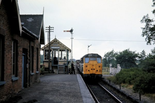 On a dull July 2nd 1970, Brush Type 2 No. 5621 (later 31197 then 31423) surrenders the token (which can be seen mid-flight, on its way to the ground) to the well-dressed signal man at Lenwade as it arrives with 8K10 from Wensum. This was a journey of approximately 30 miles (8 miles to Wroxham then a further 22 miles via Coltishall, Aylsham and Reepham) and was timetabled for just over two hours. Although the passenger service at Lenwade was withdrawn on closure of the entire Midland and Great Northern system on 28th February 1959, the signal box and station infrastructure as a whole were still in good condition at this time. Photo: John Tolson, courtesy Trevor Davis.