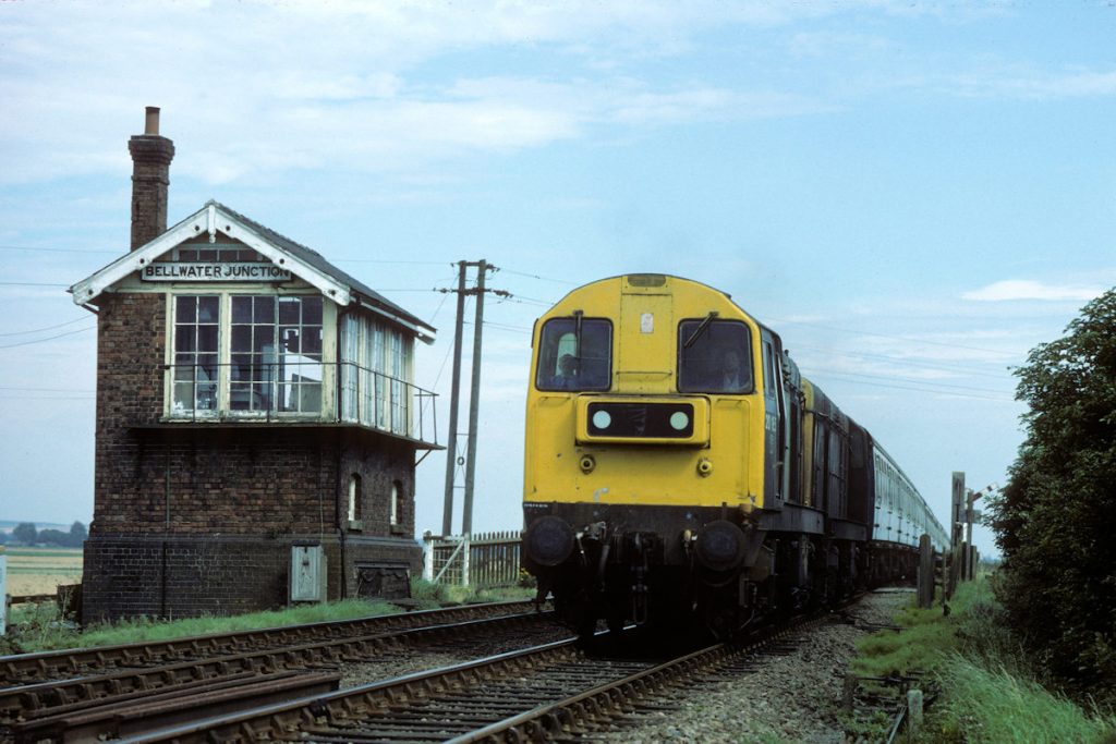19850831-BELLWATER-Jc-2018520163-1M02-12-05-SO-Skegness-Leicester-2-Alan-Jones-EW The Southern end of Bellwater Junction Signal Box had a nameboard made in the traditional Great Northern style, with individual cast letters screwed onto the board, as seen on August 31st 1985. Passing this delightful scene on their way back to Leicester are 20185 and 20163 with 1M02, the 12.05 (Summer Saturdays Only) from Skegness. Note the gradient profile of the track as it crosses Bellwater Drain and drops down on either side. Photo: Alan Jones, with permission from British Rail.