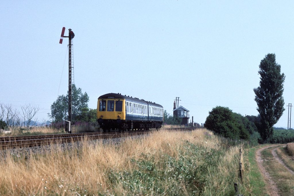 19900804-BELLWATER-Jc-08-10-Nottingham-Skegness-2-Alan-Jones-EW An unusual view of Bellwater Junction could be found from the farm track that ran along the Up side of the line, South of the Box. A two-car unit just fits between the Down Home and the Box, and on a hot and hazy August 4th 1990, Tyseley-based Class 114 set T026 (54010 and 53006) makes for a classic Lincolnshire scene with the 08.10 Nottingham to Skegness. Photo: Alan Jones.