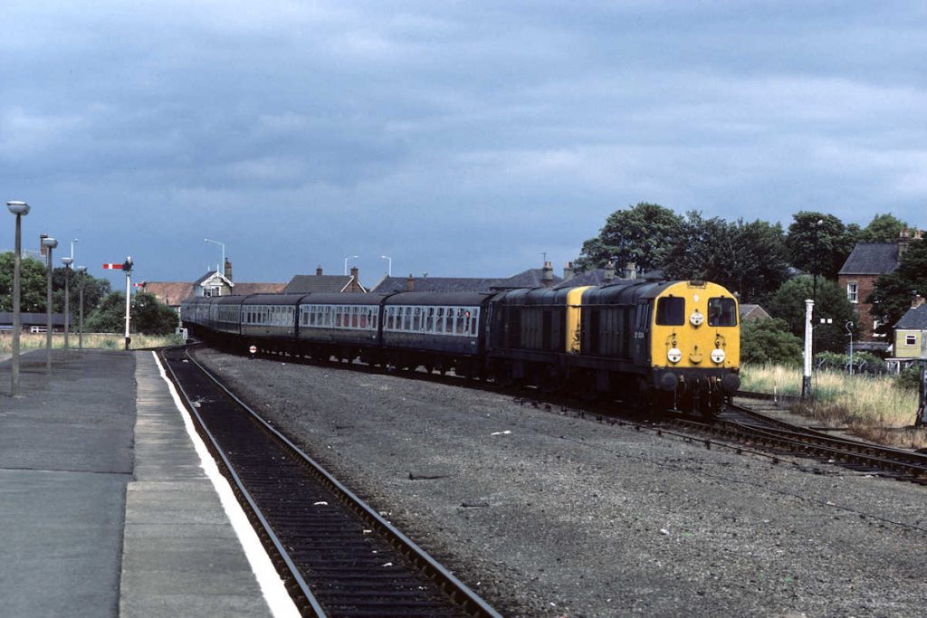 19850727-BOSTON-2003420073-1M35-12-40-SO-Skegness-Derby-Alan-Jones-EW A heavy, leaden sky presents a foreboding backdrop to English Electric Class 20s Nos. 20034 and 20073 as they pass Grand Sluice box and enter Boston station with the 12.40 (SO) Skegness-Derby on July 27th 1985. The location of the former centre roads through the station is clear, but after much rationalisation the station is now a passing place on a single line between Hubberts Bridge and Sibsey. Photo: Alan Jones.