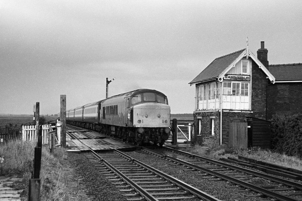 19830910-EAST-VILLE-45115-13-00-SO-Skegness-Derby-2-Alan-Jones-E3W East Ville Signal Box was in a very poor state of repair by the 1980s and was developing the distinctive 'lean' of many structures along the line. After a torrential downpour BR Class 45 No. 45115, recently displaced from the Midland Main Line by the arrival of High Speed Trains, heads past East Ville on Saturday September 10th 1983 with the 13.00 (Summer Saturdays Only) Skegness to Derby. Although signalled, East Ville was only a crossing box and not a block section, which ran from Old Leake to Bellwater Junction. Photo: Alan Jones.