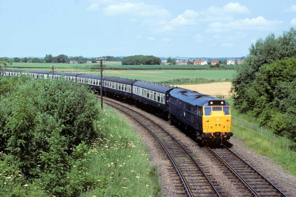 19830625-FIRSBY-31168-1D20-09-21-SO-Leeds-Skegness-2-Alan-Jones-EW The line to Firsby station used to continue round to the right, behind the locomotive and into Firsby station, but once the railway had closed and been lifted the land was soon turned back to farmland and all traces of the line disappeared. Fresh from overhaul, a very smart 31168 and its rake of Mk 1 stock squeal round the remaining part of the triangle at Frisby with the 09.21 (SO) Leeds to Skegness on June 25th 1983. Photo: Alan Jones.