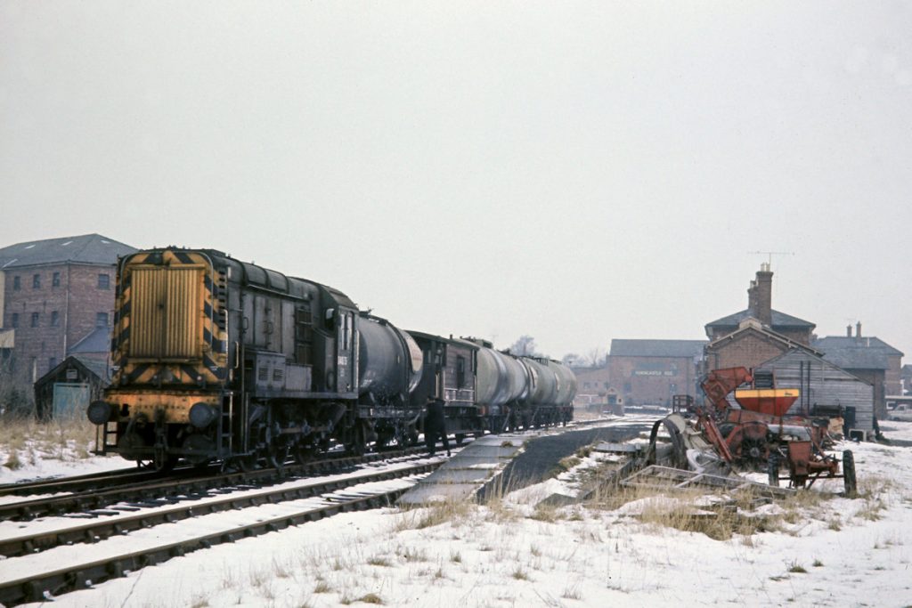 19700219-HORNCASTLE-D4075-Shunting-in-the-Yard-JMT34714-John-Tolson-E4W Having picked up a single empty tanker from the Esso siding at Horncastle on February 19th 1970, the guard is hooking it up to the LMS-style brake van of 9K77 from Holmes Yard. After this, BR Class 10 No. D4075 will shunt the formation into the oil siding (off the picture on the right) and will drop off the four loaded tanks. It will then draw out of the siding and reverse up to the far end of the station to wait time before its departure as 9K79, the 14.03 to Holmes Yard. At Greetwell Junction it will not take the Lincoln Avoiding Line but instead travel over Pelham Street Crossing and through Lincoln Central to reach Holmes Yard at 17.17. Photo: John Tolson, courtesy Trevor Davis.