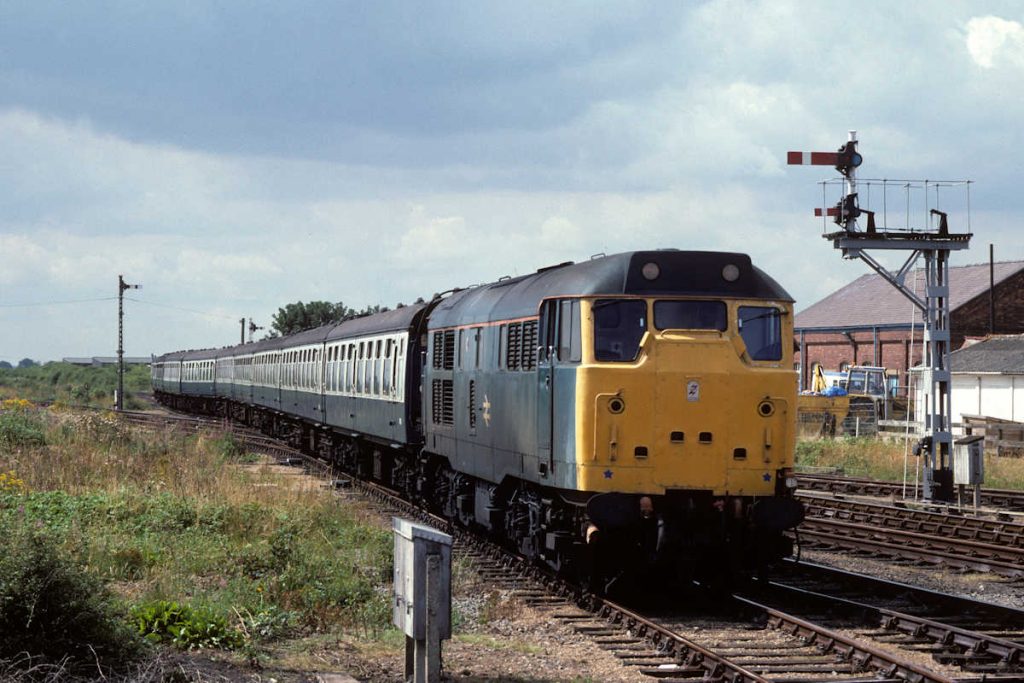 19890812-SKEGNESS-31441-Propels-08-34-SO-ex-Leeds-into-Carriage-Sidings-2-Alan-Jones-EW Brush Class 31 No. 31441 has arrived into the little used Platform 7 at Skegness with the 08.34 (SO) from Leeds on August 12th 1989. The train has been emptied and is being propelled into the carriage sidings over the slips at the throat of the station. Here, it will run round and then propel back in. The allowances for a run-round manoeuvres at Skegness were generally in the region of 40-60 minutes, so although perfectly possibly, it did require some smart work from the staff involved. Photo: Alan Jones.