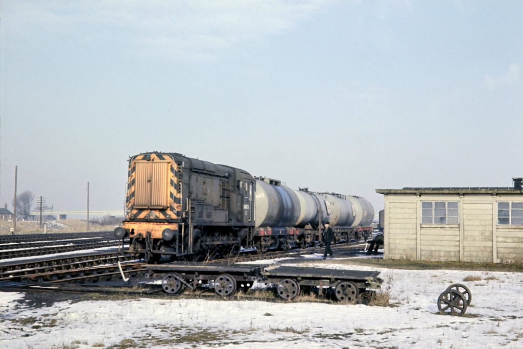 19700219-WOODHALL-Jc-D4075-10 Woodhall Junction was the point at which the 'New Line' to Bellwater Junction left the 'Loop Line' (the physical junction was South of Woodhall Junction at Coningsby Junction). It was also the junction for the Horncastle Branch which lay to the East of the station and faced East, requiring trains from the station to propel out and reverse. On a cold February 19th 1970, after a light fall of snow, Blackstone-engined Class 10 No. D4075 marshals its four fuel tanks for the Horncastle Esso depot before attaching the brake van, running round, propelling out to the junction and heading up the Branch with 9K77, the 10.19 (SX) Lincoln Holmes Yard to Horncastle. Photo: John Tolson, courtesy Trevor Davis.