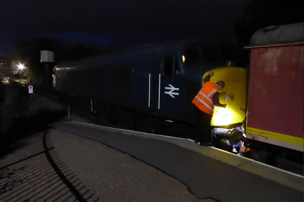 20240928-PETERBOROUGH-45041-Royal-Tank-Regiment-80327-George-James-19 In near-total darkness, the 'Night Mail' TPO has arrived at Peterborough on Saturday 28th September 2024 and 45041 'Royal Tank Regiment' is uncoupled to run round, In parallel, the essential job of loading the pies, fish and chips takes place from a nearby van, much to the delight of everyone on board. Photo: Alan Jones.