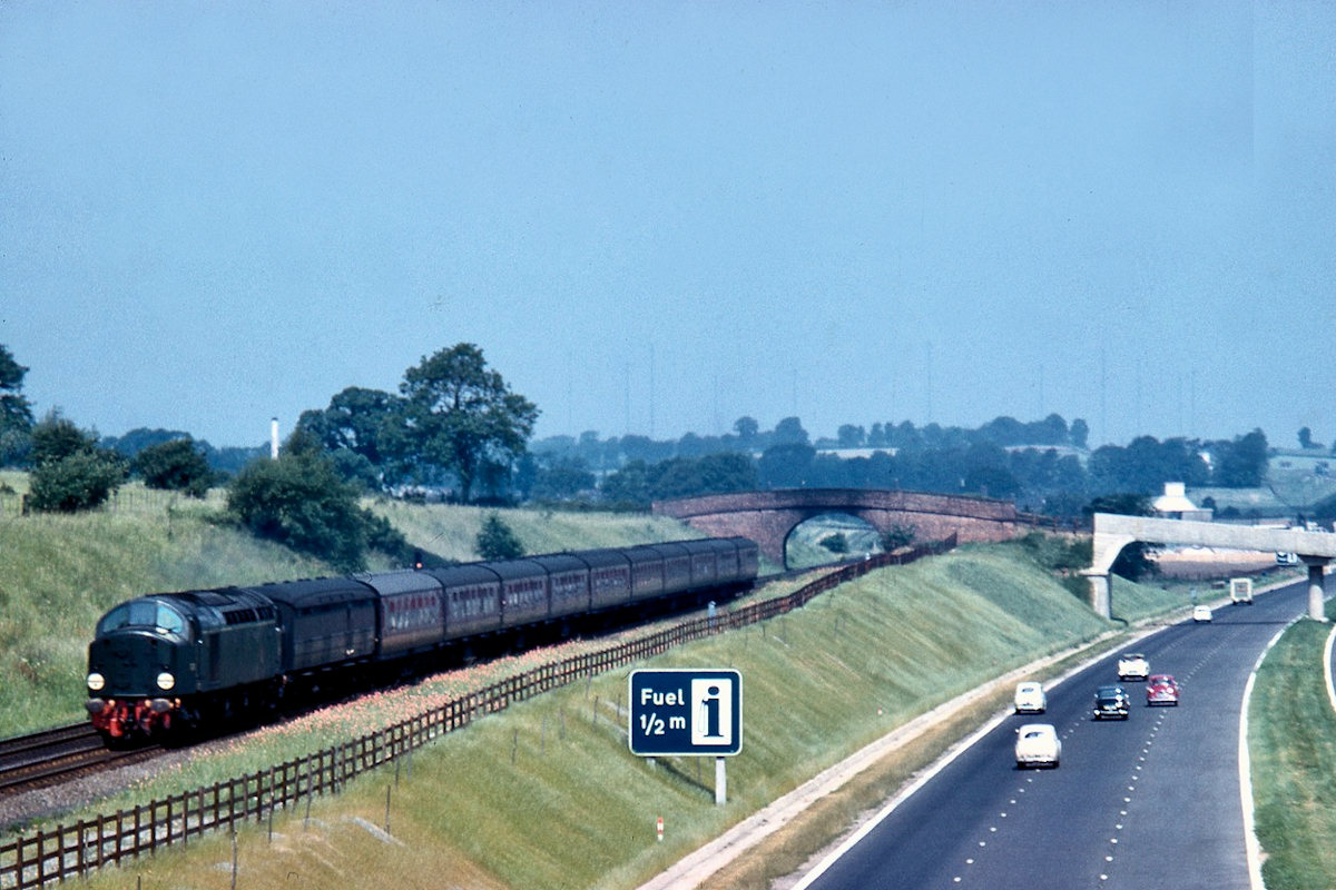 In 1960, un-named English Electric Type 4 No. D216 (named Campania in May 1962) heads South on an express to Euston, unusually with an LNER-design gangwayed brake leading the formation, alongside the newly-opened M1 motorway. In the background can be seen the Daventry radio masts where, in 1935, Robert Watson-Watt and Arnold Wilkins carried out their famous demonstration of the detection of an aircraft by radio echoes - and the invention of radar. Photo: Derek Cross, courtesy David Cross.
