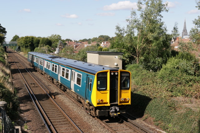Celebrity Class 313 201 in BR Blue and Grey, heads East from Chichester on the West Coastway, with the Cathedral spire in view background right. Image Credit Geoff May