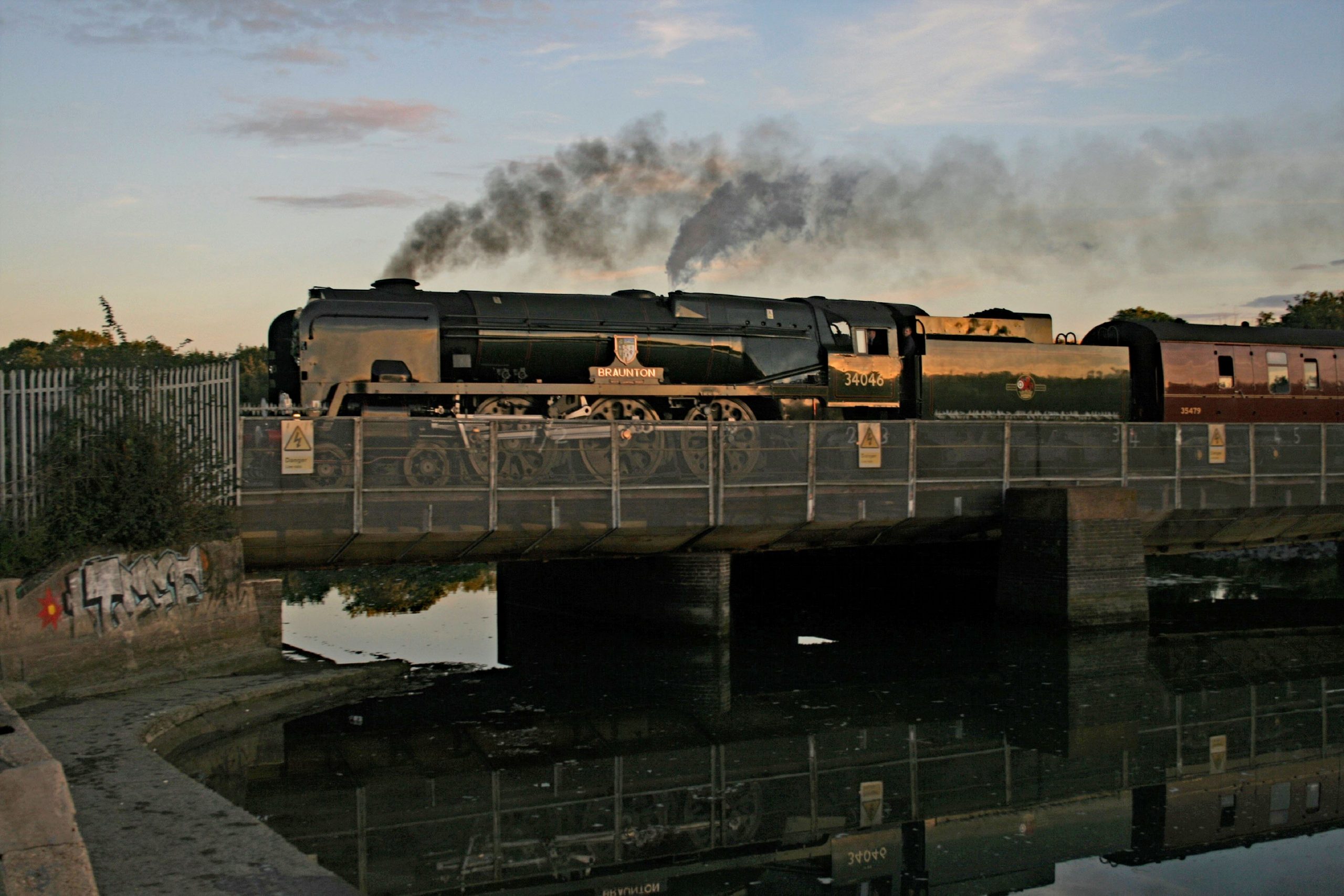 As dusk descends West Country Bulleid Pacific 34046 'Braunton' passes over Portcreek, North of Hilsea, with 1Z52 the 18:14 Chichester to Paddington, Goodwood revival return excursion. The train has reversed at Fratton with a class 47 at the head from Chichester, subsequently remaining on the rear through to London. 18 September 2022. Image Credit John Barrowdale.