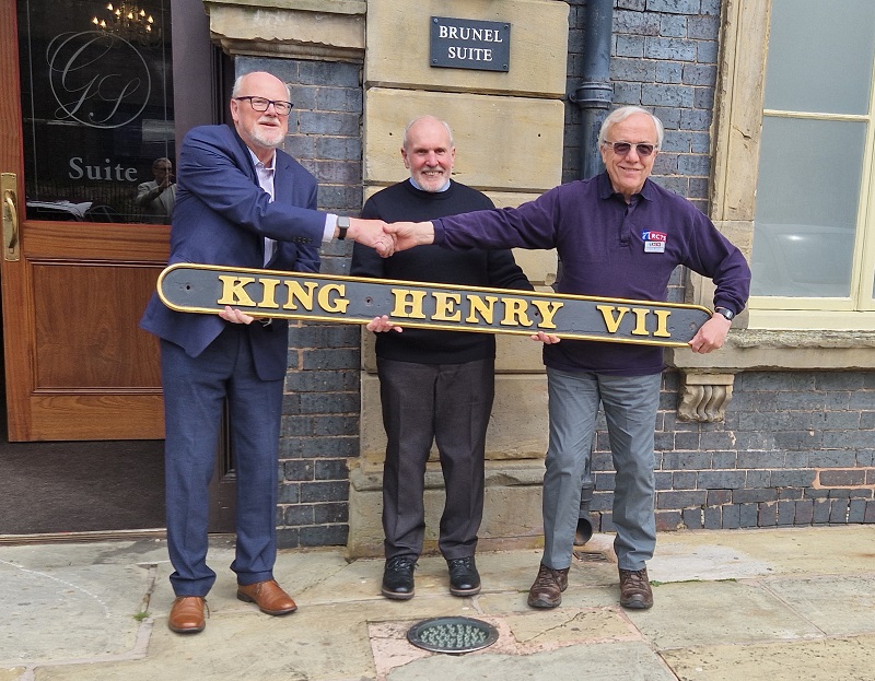 Retiring Chairman Callum MacLeod (right) shaking hands with Chairman-elect James Milne (left), both flanking President Rev Canon Brian Arman.  All are holding an unusual straight nameplate from GWR 6000 Class 6014 King Henry VII, which is owned by the Society.